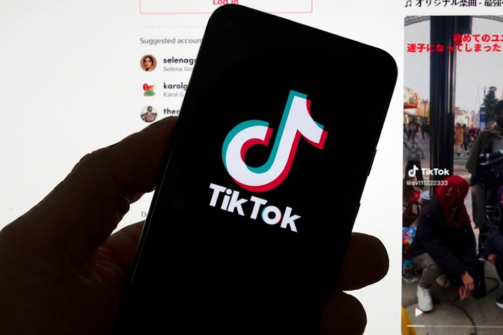 The TikTok logo is seen on a mobile phone in front of a computer screen which displays the TikTok home screen, Saturday, March 18, 2023, in Boston. 