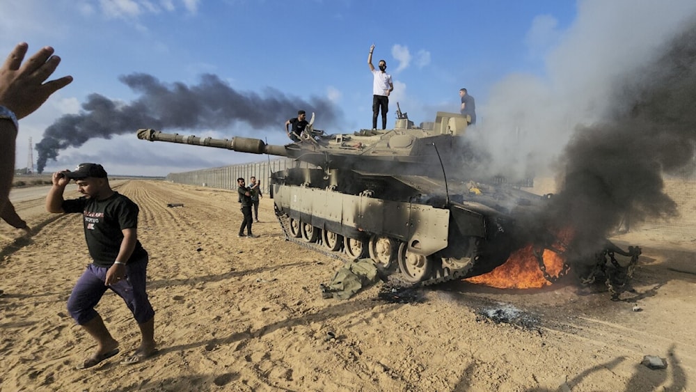 Palestinians celebrate by a destroyed Israeli tank at the Gaza Strip fence east of Khan Younis southern on Saturday, October 7, 2023. (AP)