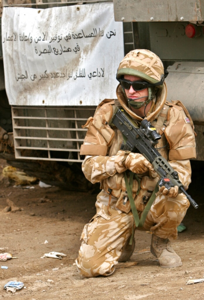 A British soldier, part of the multinational mission in Iraq, kneels infront of a sign reading 