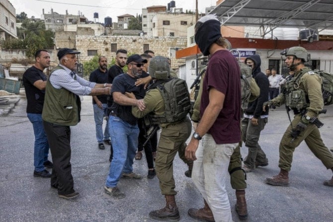 A masked Israeli settler stands by while Palestinians and Israeli soldiers scuffle during clashes in the town of Huwara in the occupied West Bank. (AFP)