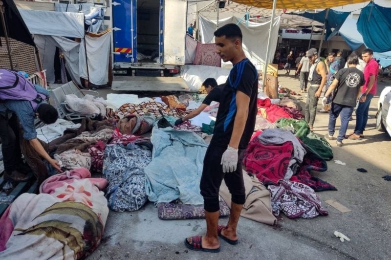 A man is looking for the bodies of family members killed in bombardment that hit a school housing displaced Palestinians, as they lie on the ground in the yard of al-Shifa Hospital in Gaza City on Nov. 10, 2023. (AFP)