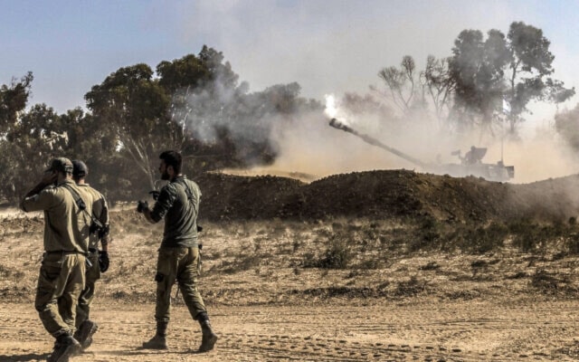 Israeli invading soldiers walk near a stationed self-propelled artillery howitzer firing rounds from a position near the border with the Gaza Strip on November 6, 2023. (AFP)