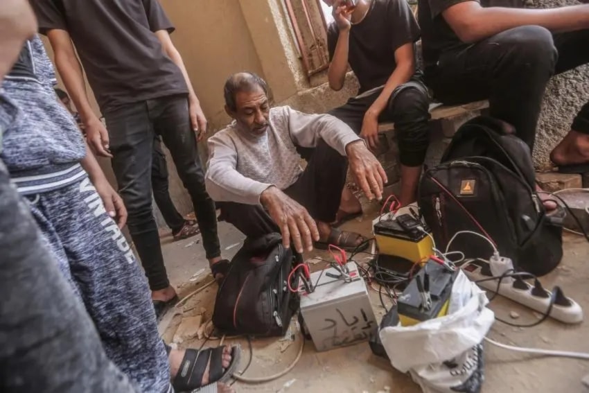 Palestinians in Khan Yunis, Gaza, use car batteries to charge their mobile phones, October 23, 2023. (AP)