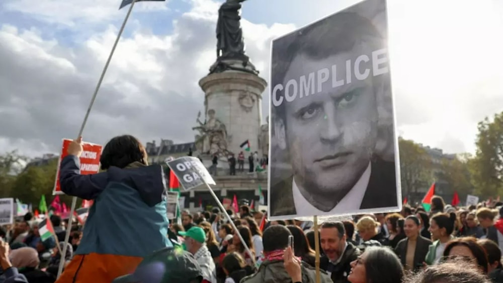 Protesters hold up a sign condemning French President Emmanuel Macron at a rally in Paris on 22 October 2023 (AFP)