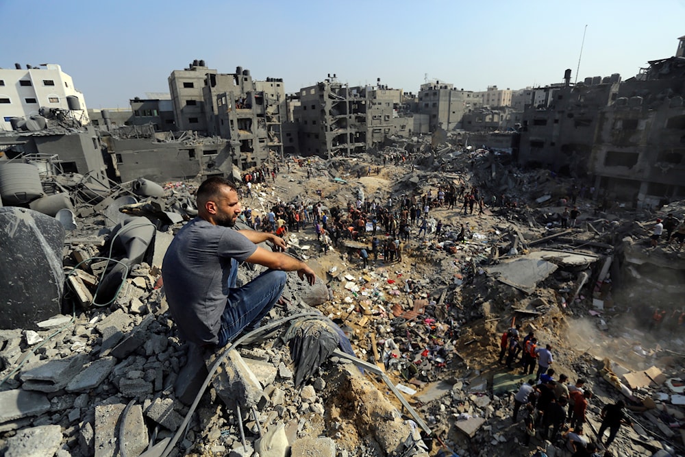 A man sits on the rubble as others wander among debris of buildings that were targeted by Israeli airstrikes in Jabalia refugee camp, northern Gaza Strip, Wednesday, Nov. 1, 2023. (AP)