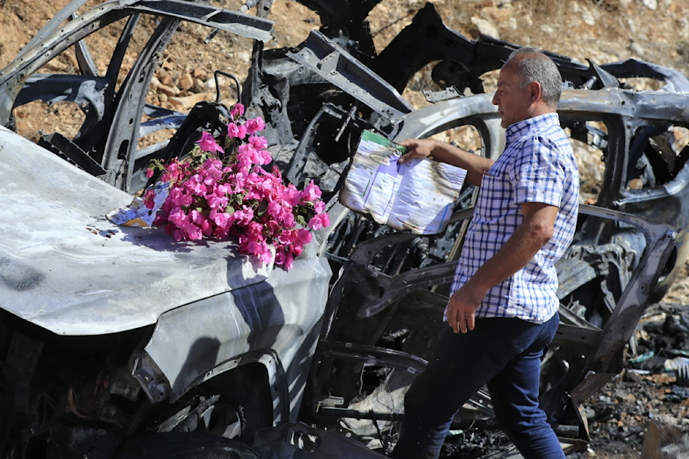 Samir Ayoub, the uncle of the three children who were killed by an Israeli airstrike puts flowers and a burned book on their car in Ainata, South Lebanon on November 6, 2023. (AP)