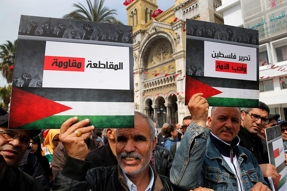 Tunisian protesters hold placards showing the Palestinian flag and Arabic that reads, 