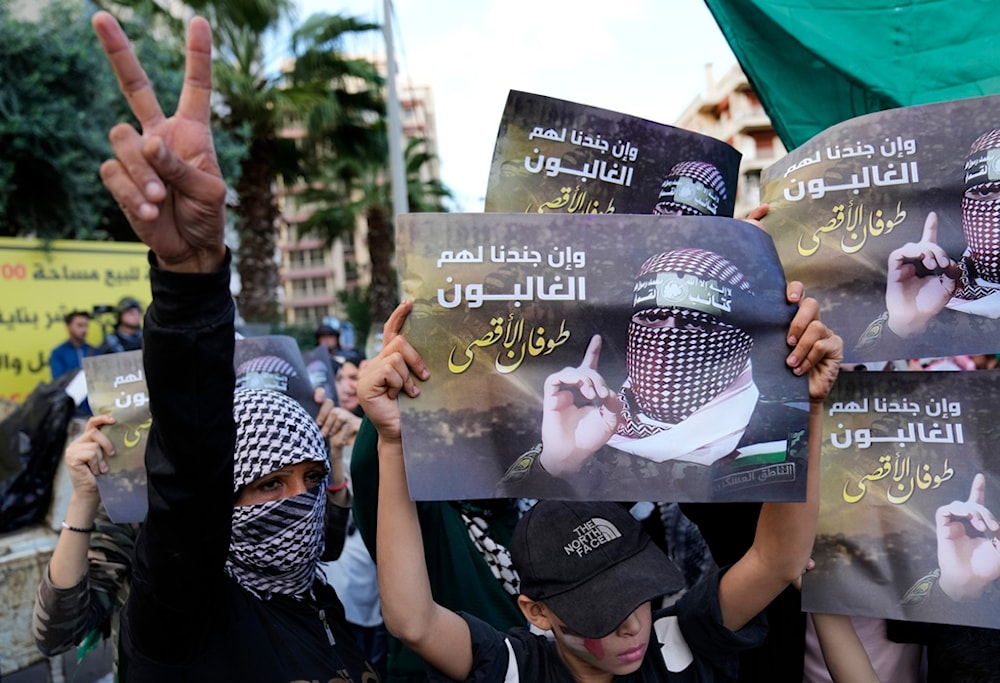 A Palestinian protester flashes a victory sign, as other hold up portraits of al-Qassam Brigades spokesperson Abu Obeida during a pro-Palestine protest near the the Egyptian embassy in Beirut, Lebanon, November 18, 2023 (AP)