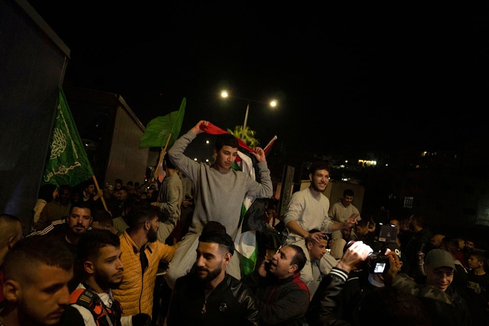 Former Palestinian prisoners who were liberated from the Israeli occupation's prisons, fly Palestinian and Hamas flags while they are carried on the shoulders upon their arrival in Beituna, occupied Palestine, November 24, 2023 (AP)