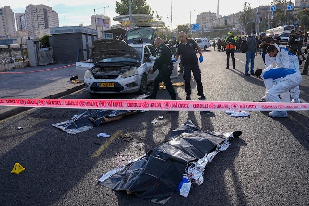 An Israeli police officer aims his firearm at the body of one of the men who carried out an operation in occupied al-Quds, occupied Palestine, November 30, 2023 (AP)