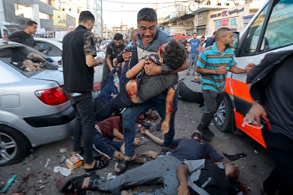 A bereaved man carries a child over the bodies of dead and injured Palestinians lying on the ground following an Israeli airstrike outside the entrance of the al-Shifa hospital in Gaza City, November 3, 2023 (AP)