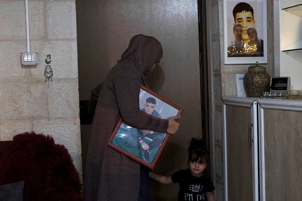 Maysoon Manasra carries a portrait of her son, Ahmad Manasra, who has been imprisoned by the Israeli occupation since he was 13 years old, with her daughter in their home in occupied al-Quds, Tuesday, Nov. 8, 2022.(AP)