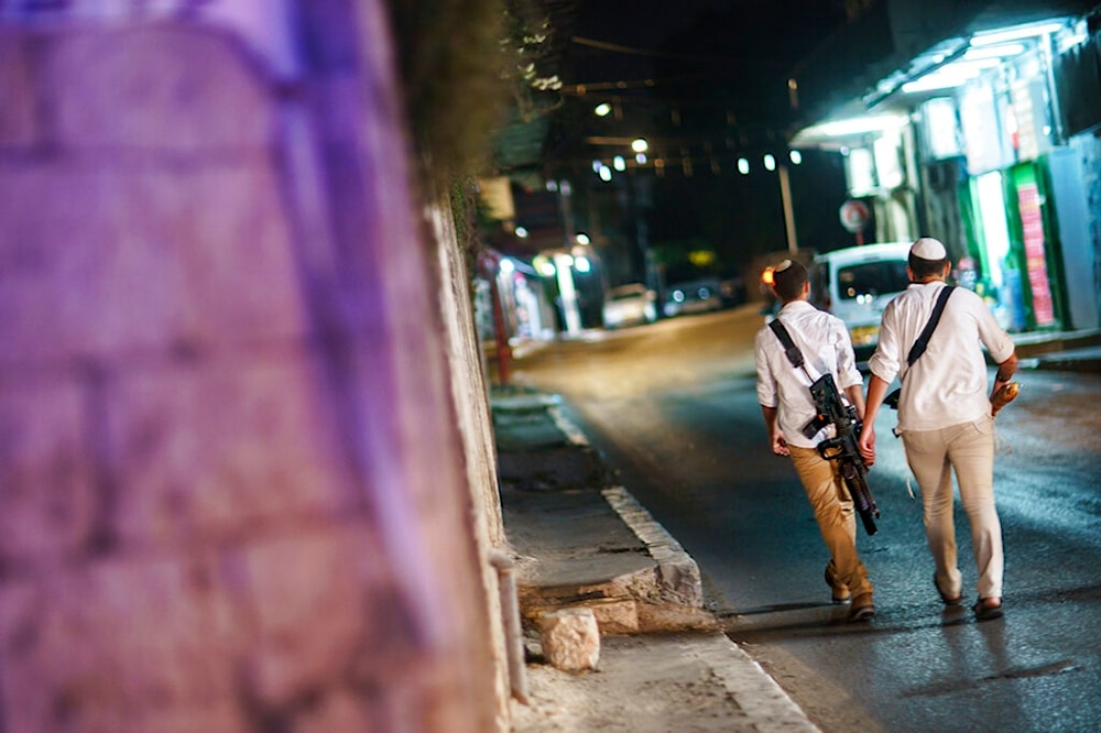 Armed Israeli settlers walk through the street with guns in the mixed Arab-Jewish town of al-L, occupied city of al-Lydd, Friday, May 28, 2021. (AP)