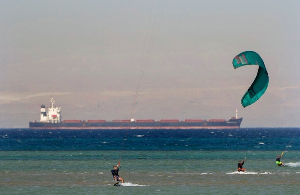 Egyptian holiday-makers play water ski as a cargo container ship, crosses the Gulf of Suez towards the Red Sea at al Sokhna beach in Suez, 127 kilometers (79 miles) east of Cairo, Egypt, Friday, Aug. 26, 2022