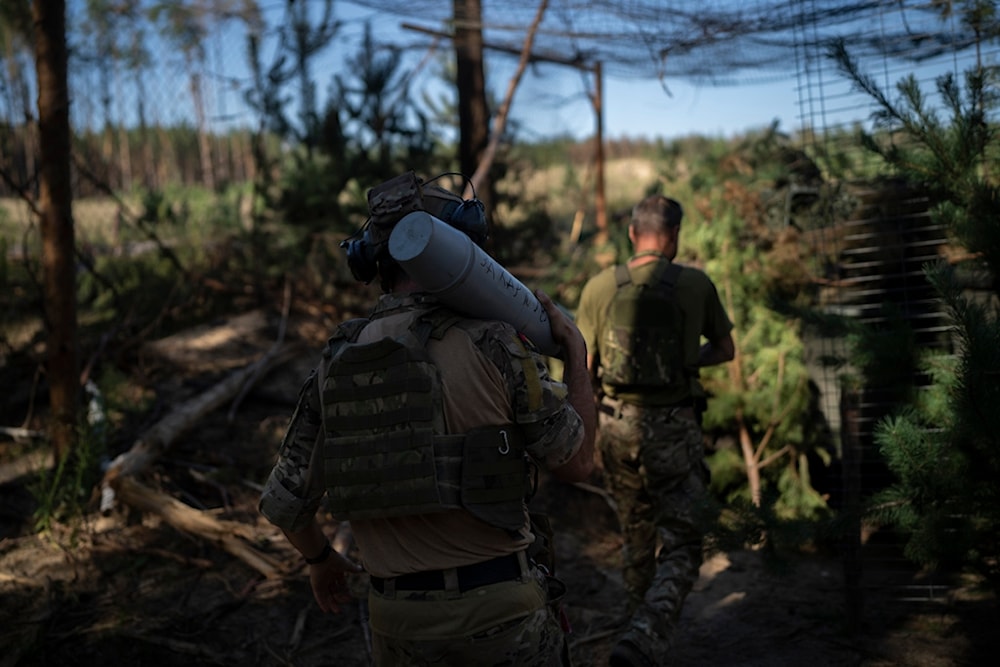 A Ukrainian soldier carries a shell towards a howitzer on the front line in the outskirts of Lyman, Donbass region, Tuesday, Aug. 15, 2023 (AP Photo/Bram Janssen)