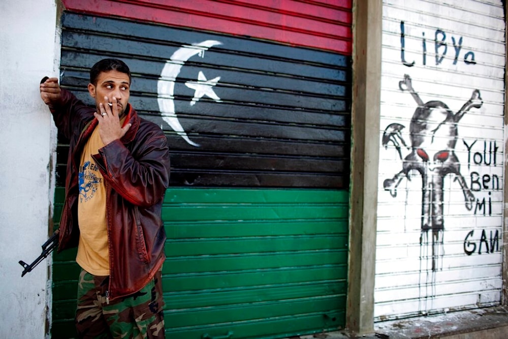 A rebel soldier stands guard next to the place where artist Salhen Obaidi paints a portrait of Omar Mukhtar, the leader who fought against the Italian occupation in Libya, in downtown Benghazi, Libya, Sunday, May 15, 2011 (AP)