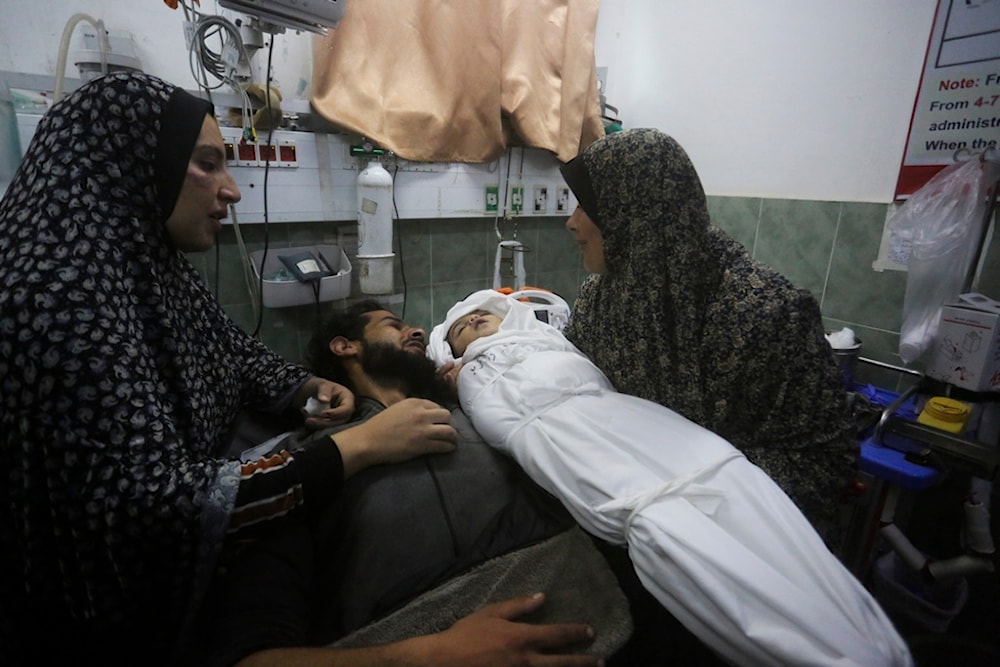 A Palestinian woman shows the body of her grandchild, her father after it was killed in the Israeli bombardment of the Gaza Strip outside a morgue in Rafah, Tuesday, Dec. 19, 2023. (AP Photo/Hatem Ali)