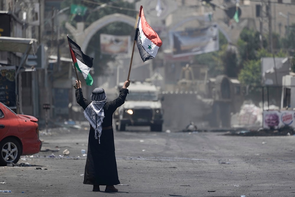 A Palestinian man waves Palestinian and Syrian flags in front of an Israeli army vehicle during a military raid in the Jenin refugee camp, a militant stronghold, in the occupied West Bank, Tuesday, July 4, 2023. (AP)