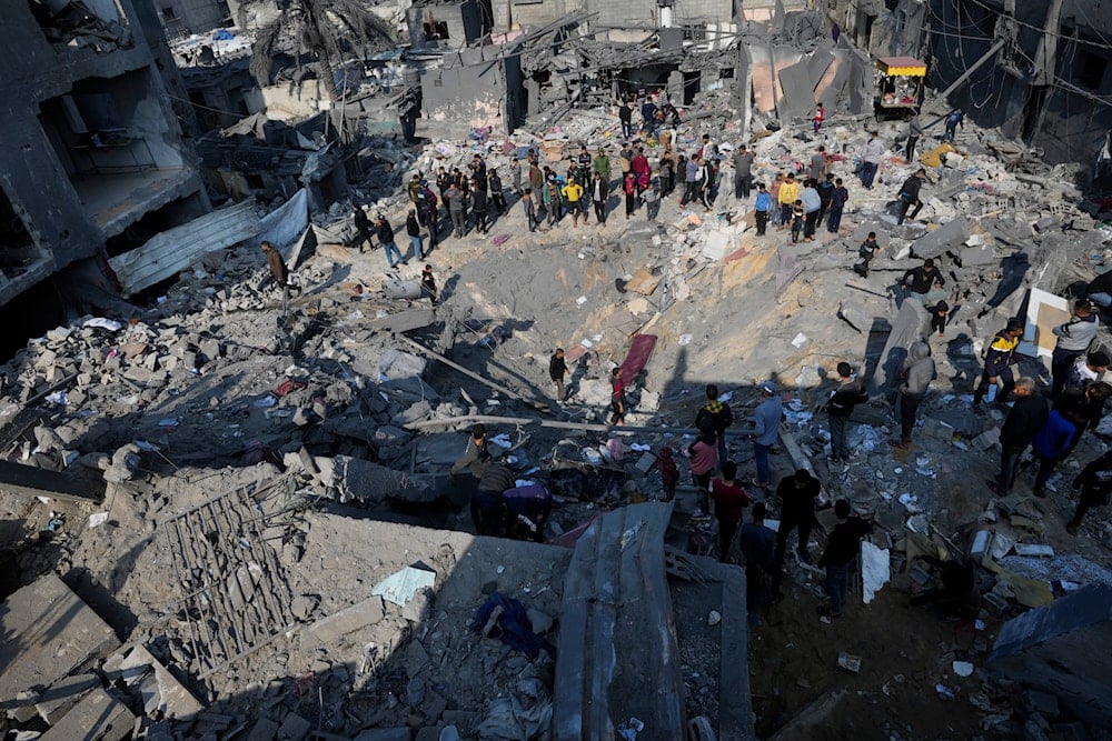 Palestinians look at the destruction of the al-Gatshan family building after an Israeli strike in Nuseirat refugee camp, central Gaza Strip, on December 18, 2023 (AP)