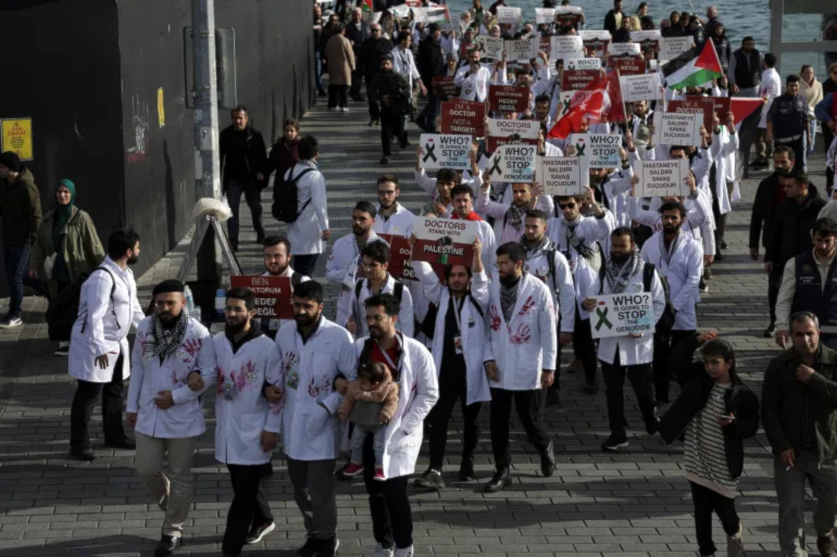 Turkish doctors and medical students wearing white coats with red hand prints and holding signs and placards in solidarity with Gaza as they march in Istanbul, Turkey on December 2, 2023 (Social Media)