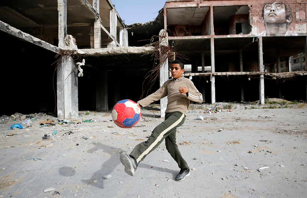 A boy plays football next to a mural painted by Palestinian artist Ali Al-Jabali on the remains of a building in April 30, 2019. (AP)