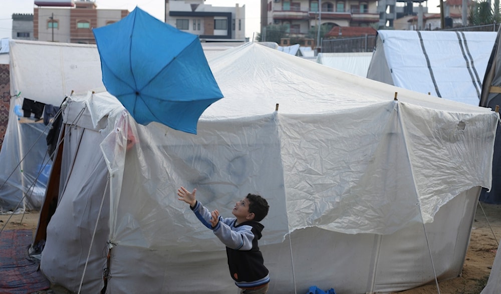 A Palestinian boy displaced by the Israeli genocidal war plays with an umbrella outside a makeshift tent in Rafah, Gaza Strip, occupied Palestine, Tuesday, Jan. 2, 2023. (AP)