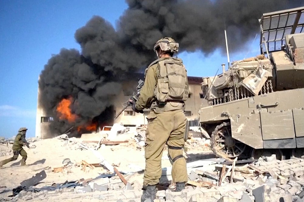 Israeli invading soldier holds a weapon as smoke billows from explosion in the background, in Gaza City, Nov. 14, 2023 (AP)