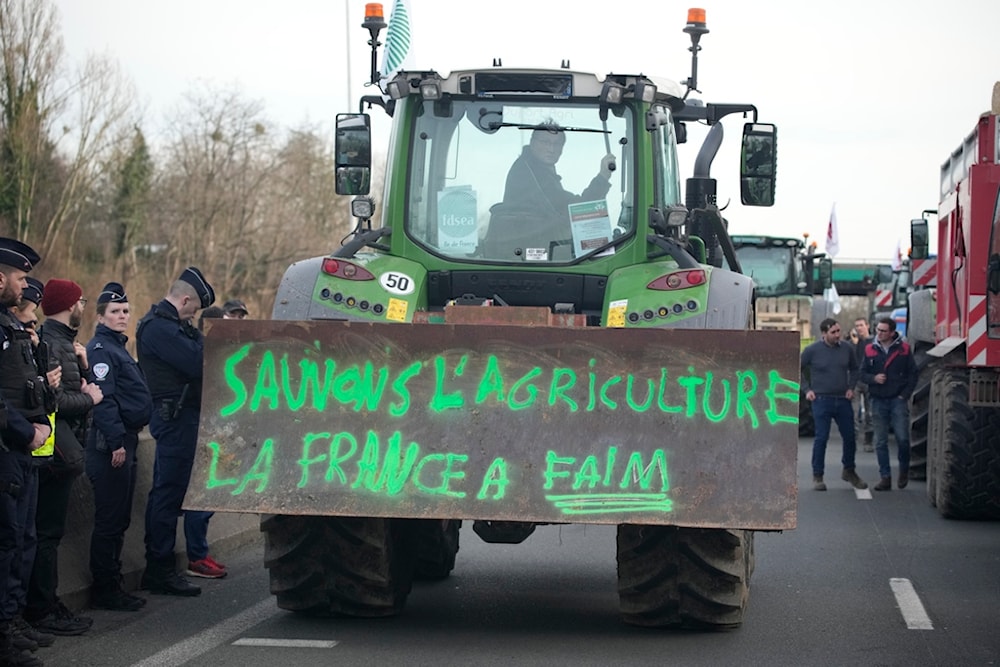 Police forces watch a farmerdriving his tractor with inscription 