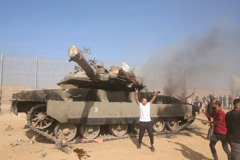 Gazans celebrate by a burning Israeli tank at the separation wall, Gaza Strip on Saturday, Oct. 7, 2023 (AP)