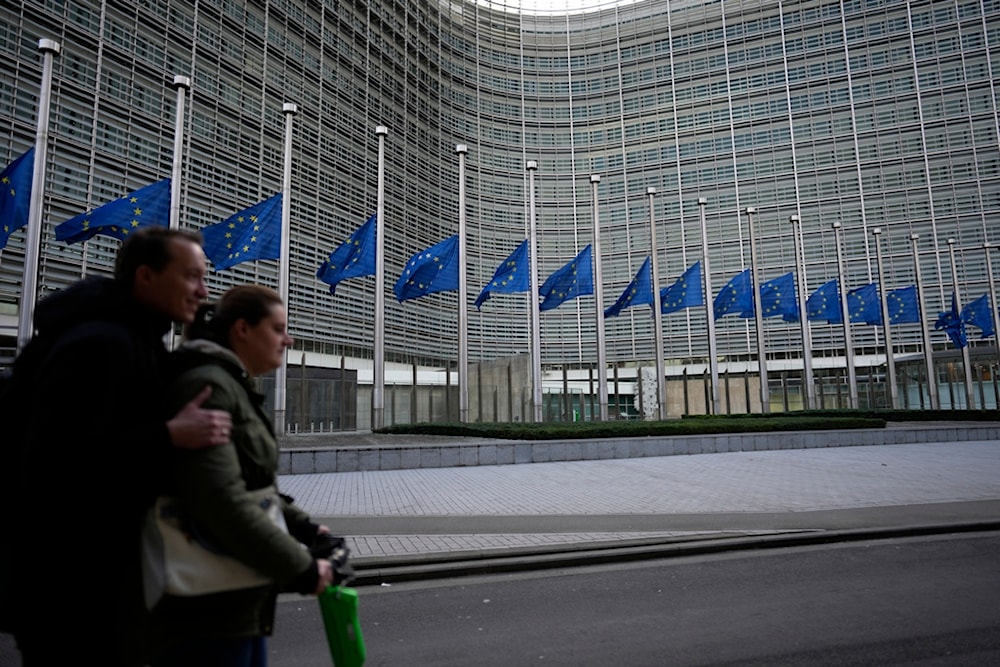Two people ride on a scooter as EU flags flap in the wind at half staff, in remembrance of former European Commission President Jacques Delors, in front of EU headquarters in Brussels, Dec. 28, 2023. 