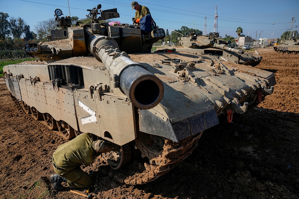 Israeli soldiers work on their tank in a staging area at the Gaza envelope in southern occupied Palestine, January 4, 2024 (AP)
