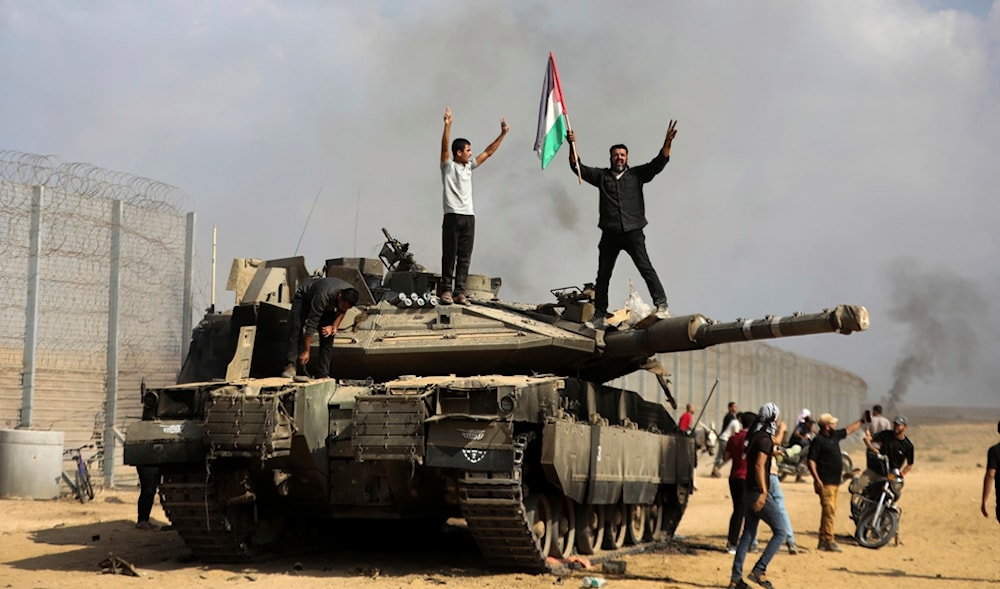 Palestinians wave their national flag and celebrate by a destroyed Israeli tank at the southern Gaza Strip fence east of Khan Younis, occupied Palestine, on Saturday, Oct. 7, 2023. (AP)