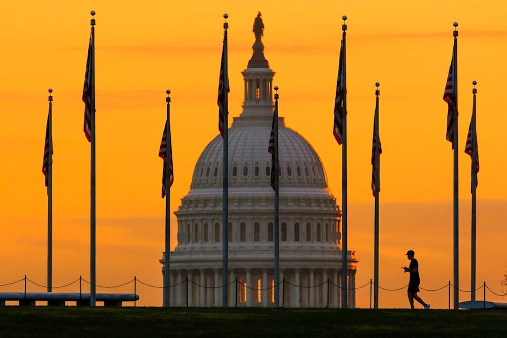 An early morning pedestrian is silhouetted against sunrise as he walks through the U.S. Flags on the National Mall and past the US Capitol Building in Washington Monday, Nov. 7, 2022. (AP Photo)