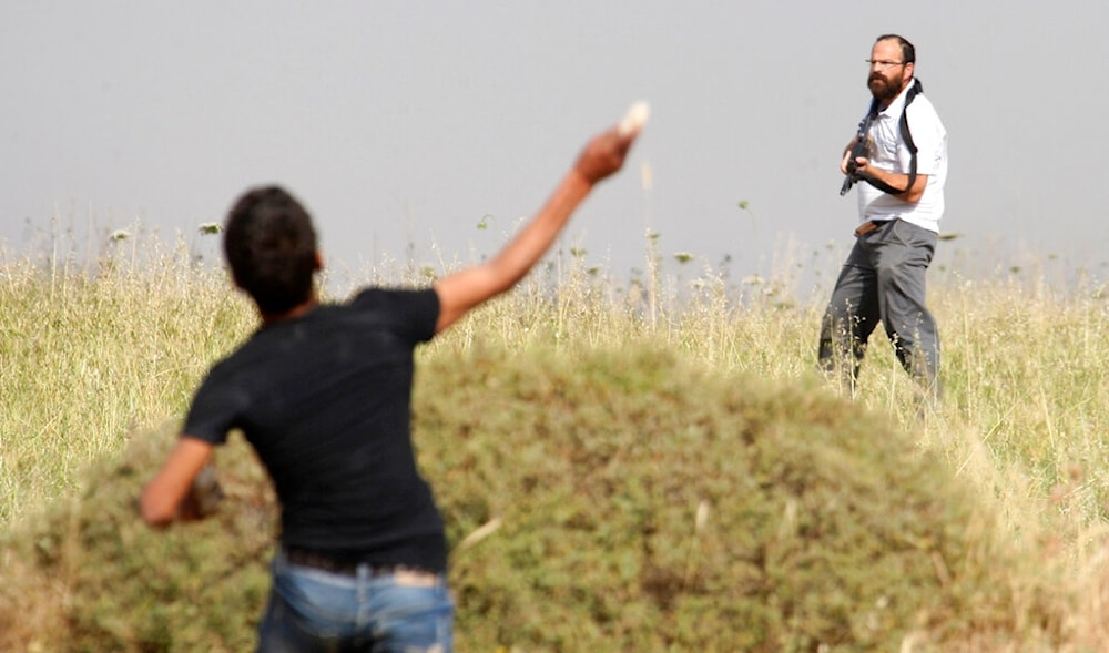 In this May 19, 2012 file photo, a Palestinian throws a stone at an armed Israeli settler invading a Palestinian village in the occupied West Bank, Palestine. (AP)