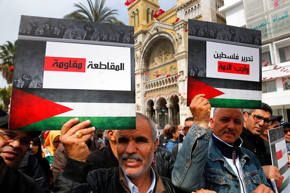 Protesters hold placards showing the Palestinian flag and Arabic that reads, 