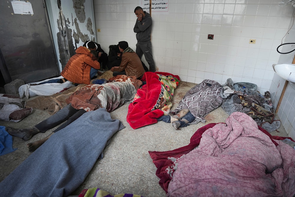Palestinians kneel next to the bodies of relatives killed in the Israeli bombardment of the Gaza Strip, inside a morgue of Al Aqsa hospital, in Deir al Balah, Gaza Strip, Monday, Feb. 12, 2024. (AP)