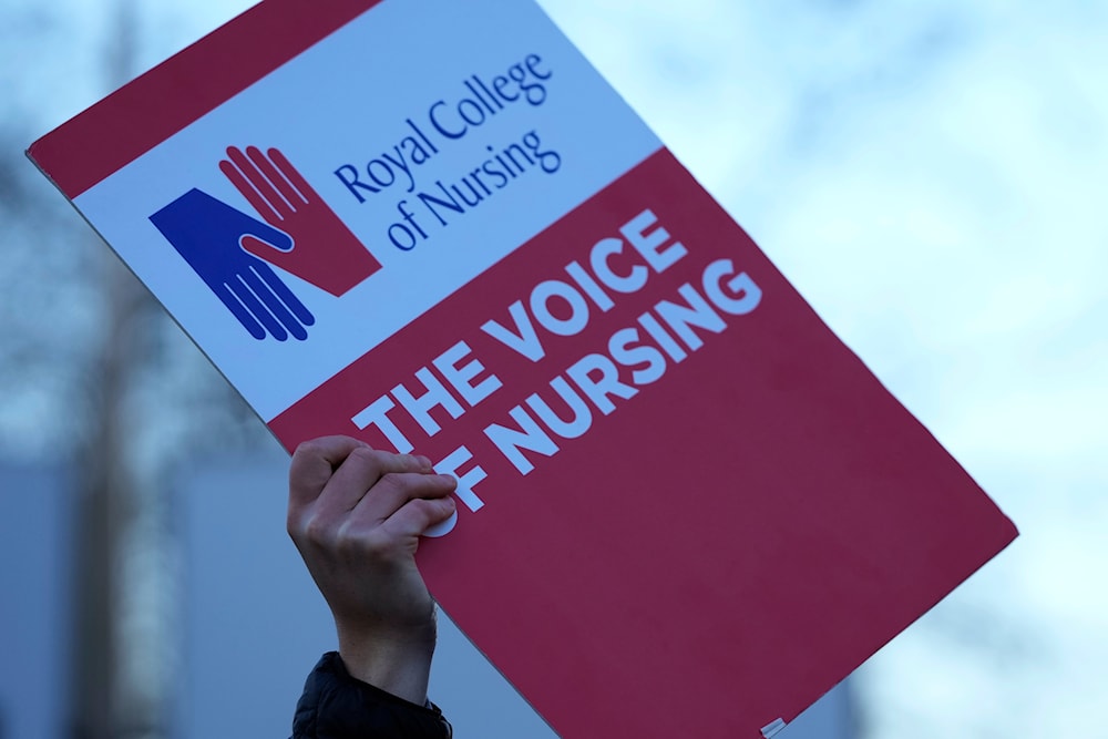 A demonstrator holds up a placard in support of the strike by nurses outside St Thoma's Hospital in London, Tuesday, Dec. 20, 2022(AP)
