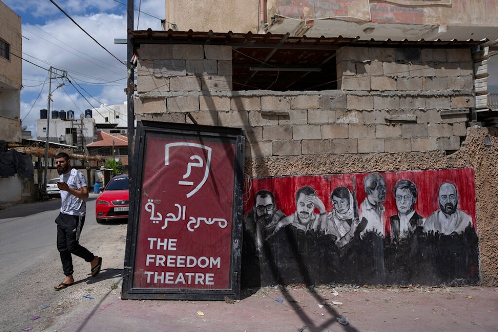 A Palestinian man walks past graffiti that depicts late notable Palestinians, at the entrance of the Freedom Theatre, April 12, 2022 (AP)