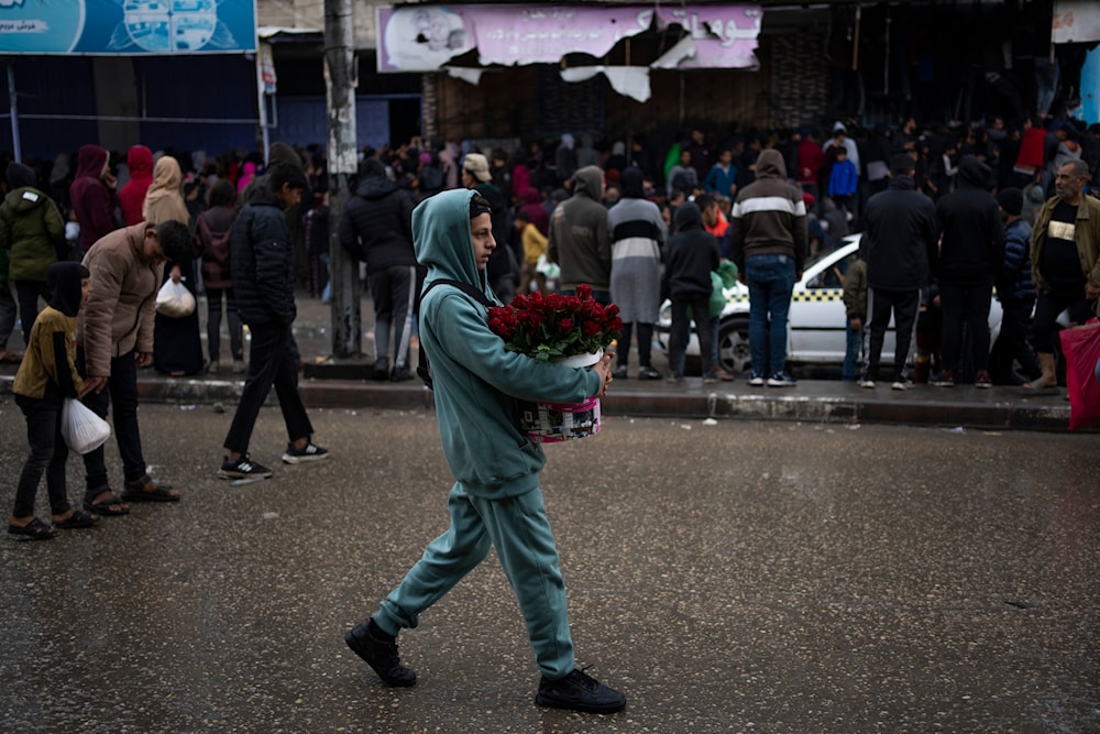 A Palestinian youth carries a bucket with roses at the market in Rafah on Sunday, Feb. 18, 2024. (AP)