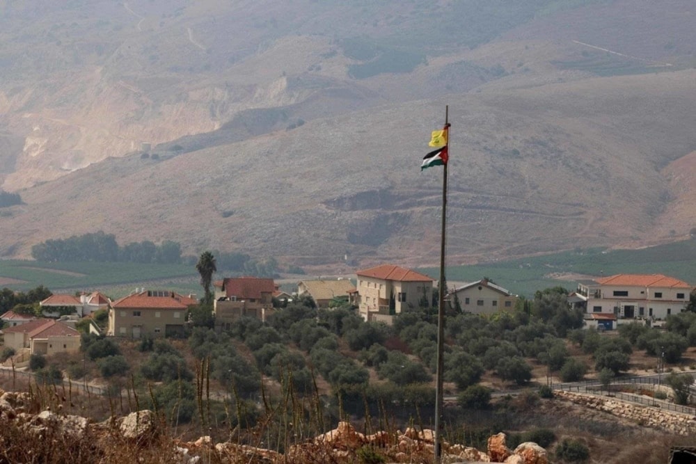 The flags of Palestine (bottom) and Hezbollah (top) flutter in the foreground in the southern Lebanese plain of Khiam with the northern Israeli settlement of 