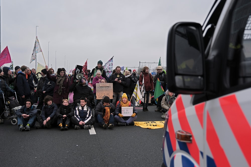 Climate activists sit on the ground, in front of a police van, blocking the main highway around Amsterdam near the former headquarters of an ING bank to protest its financing of fossil fuels, Saturday, Dec. 30, 2023.(AP)