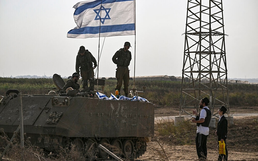 Israeli occupation forces on an armored vehicle speak with an ultra-Orthodox Haredi jew as they deploy near occupied territories bordering Gaza Strip on October 24, 2023. (AFP)