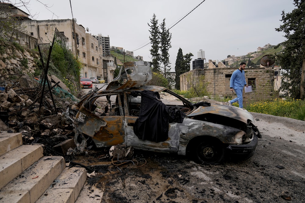 A man passes by a car destroyed by an IOF raid in the occupied West Bank in Jenin refugee camp on Wednesday, March 27, 2024. (AP)