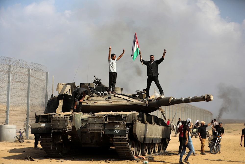 Palestinians wave the Palestinian flag and celebrate by a destroyed Israeli tank at the southern Gaza Strip fence east of Khan Younis on Saturday, Oct. 7, 2023. (AP)