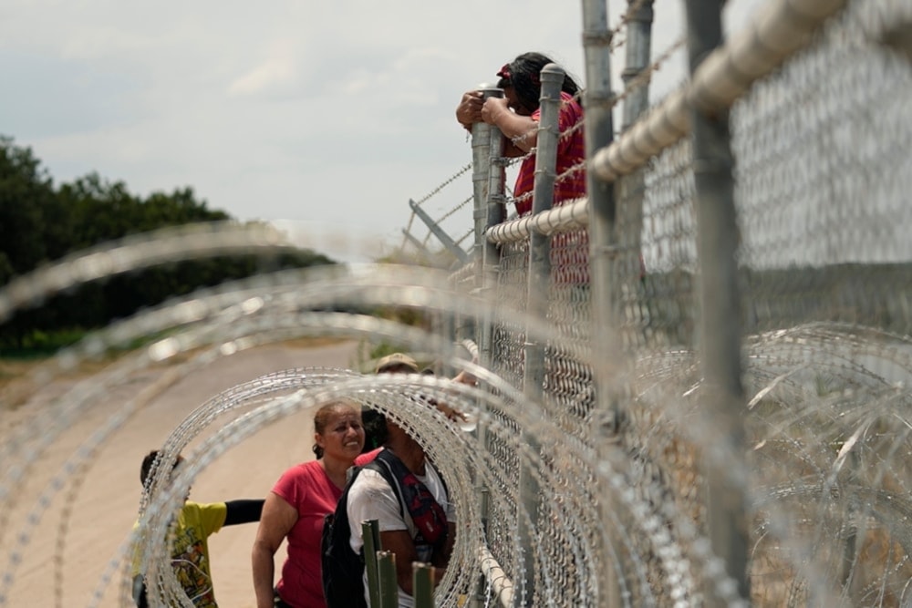 Migrants who crossed the Rio Grande from Mexico into the US climb a fence with barbed wire and concertina wire in 2023, in Eagle Pass, Texas. (AP)