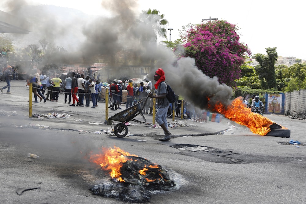 A man pushes a wheelbarrow past burning tires during a protest demanding the resignation of Prime Minister Ariel Henry, in Port-au-Prince, Haiti, Thursday, March 7, 2024.