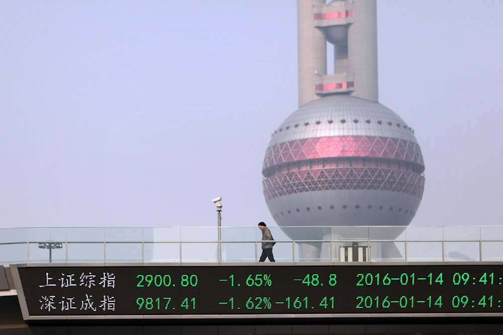 A pedestrian walks across an elevated bridge showing index figures for the Shanghai, top, and Shenzhen, bottom, stock exchanges in Shanghai, January 14, 2016. (AP)
