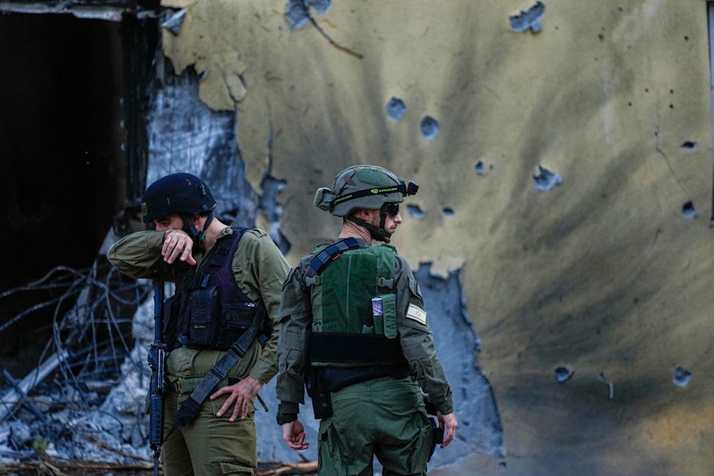Israeli occupation forces walk past houses destroyed in Kibbutz 