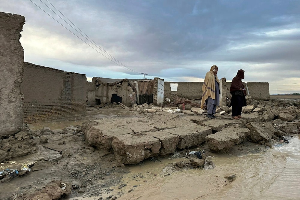 People stand over the wall of their damaged house caused by flooding due to heavy rains in the area near Chaman, Pakistan, Thursday, April 18 2024 (AP)