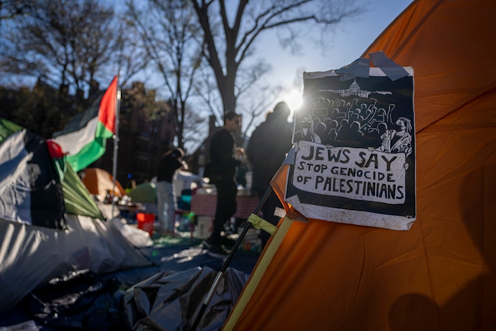 Students protesting against the war on Gaza stand next to a Palestinian flag and tents at an encampment in Harvard Yard, at Harvard University in Cambridge, Mass., on Thursday, April 25, 2024 (AP Photo/Ben Curtis)